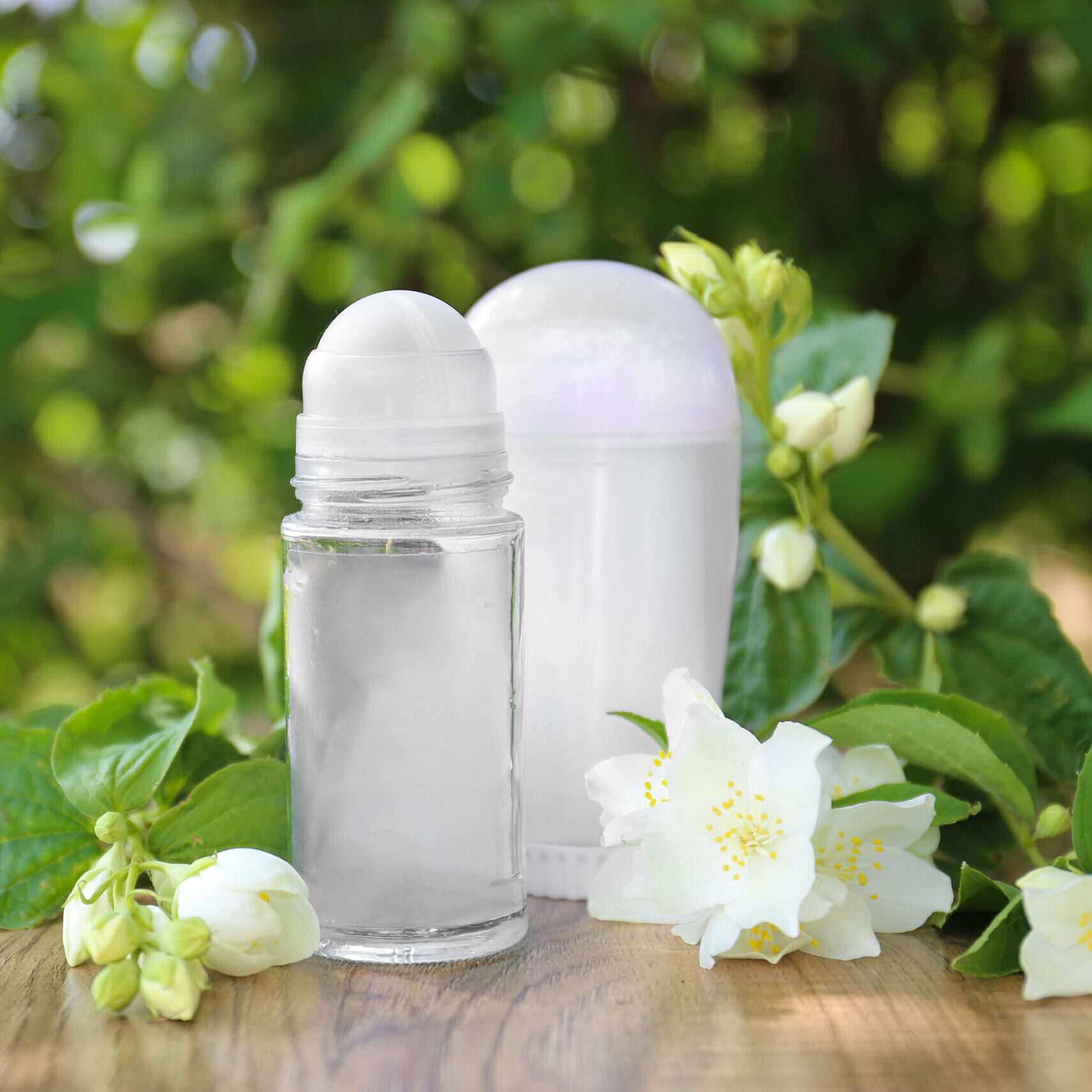 deodorant with white flowers and green leaves on a wooden table